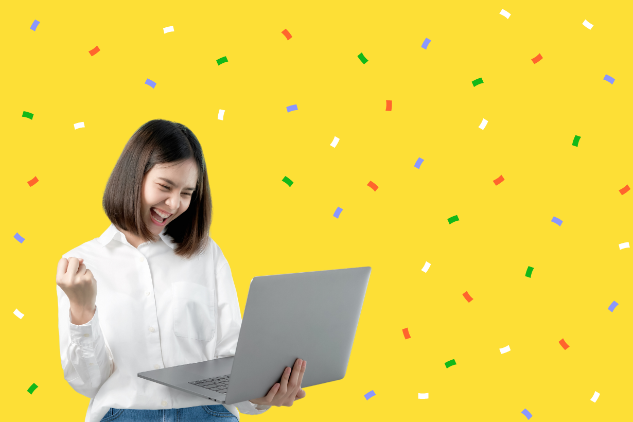 Joyful young woman in a white blouse using a laptop and celebrating, with a bright yellow background sprinkled with multicolored confetti.