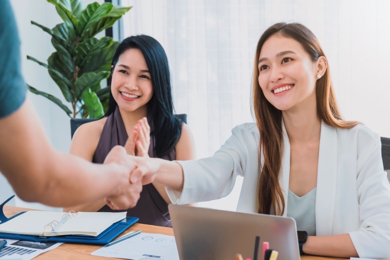 Two smiling women in a business meeting shaking hands with a person.